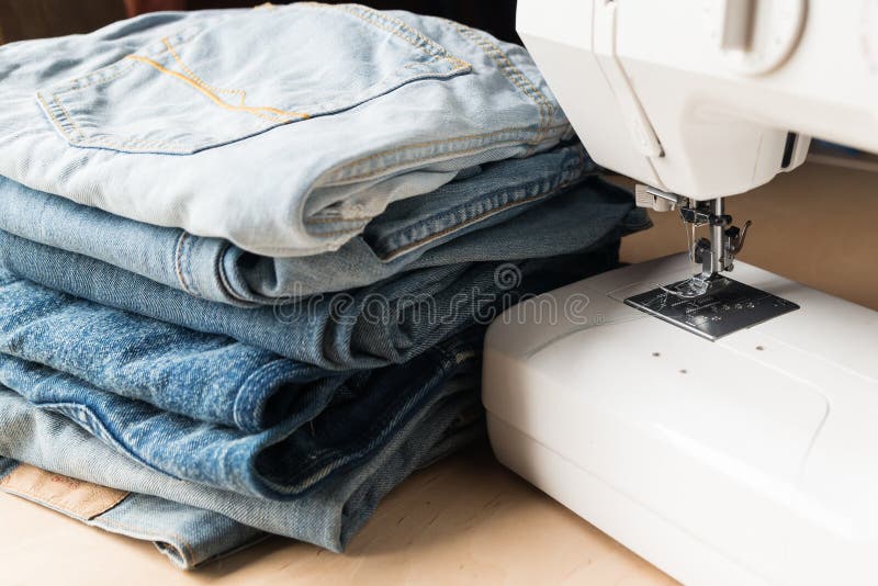 a stack of old torn jeans and a sewing machine on a wooden table stock photography